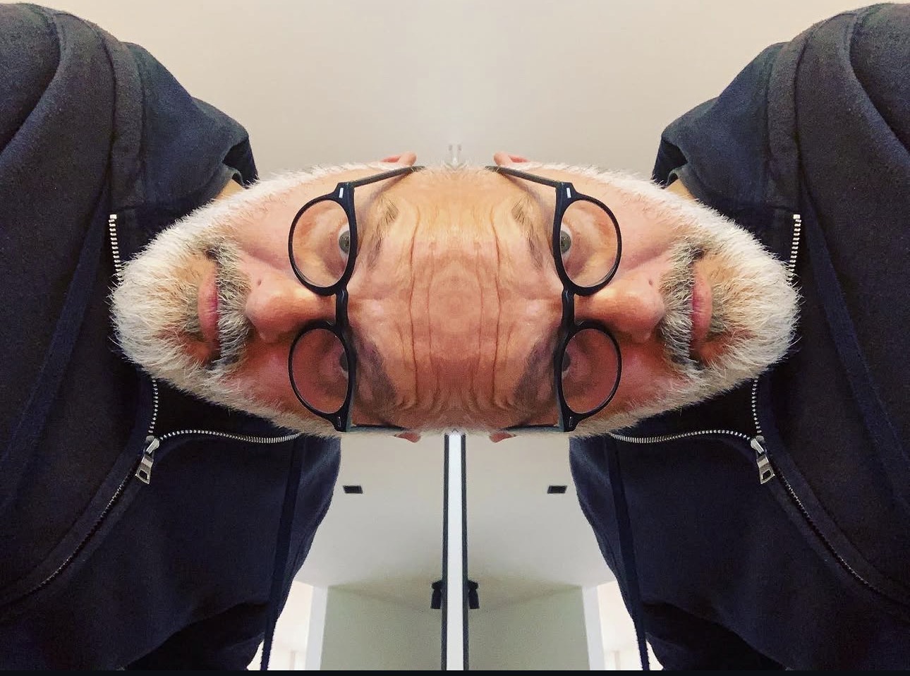 A mirrored self-portrait: his face doubled across the glass edge of a table.